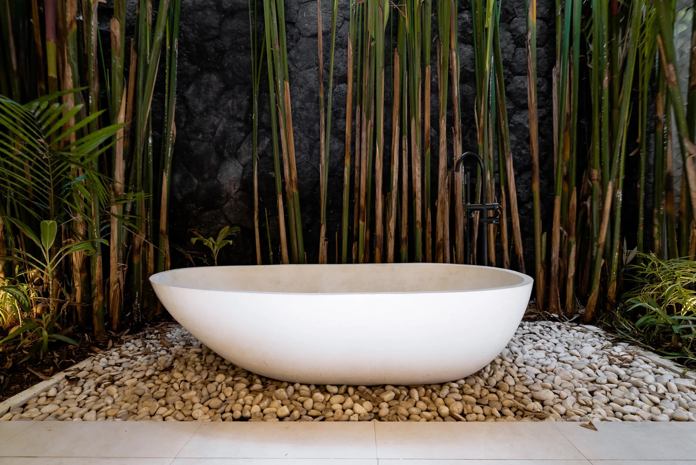 A stone bathtub set against growing bamboo at Casa Petak, a finished Balitecture villa