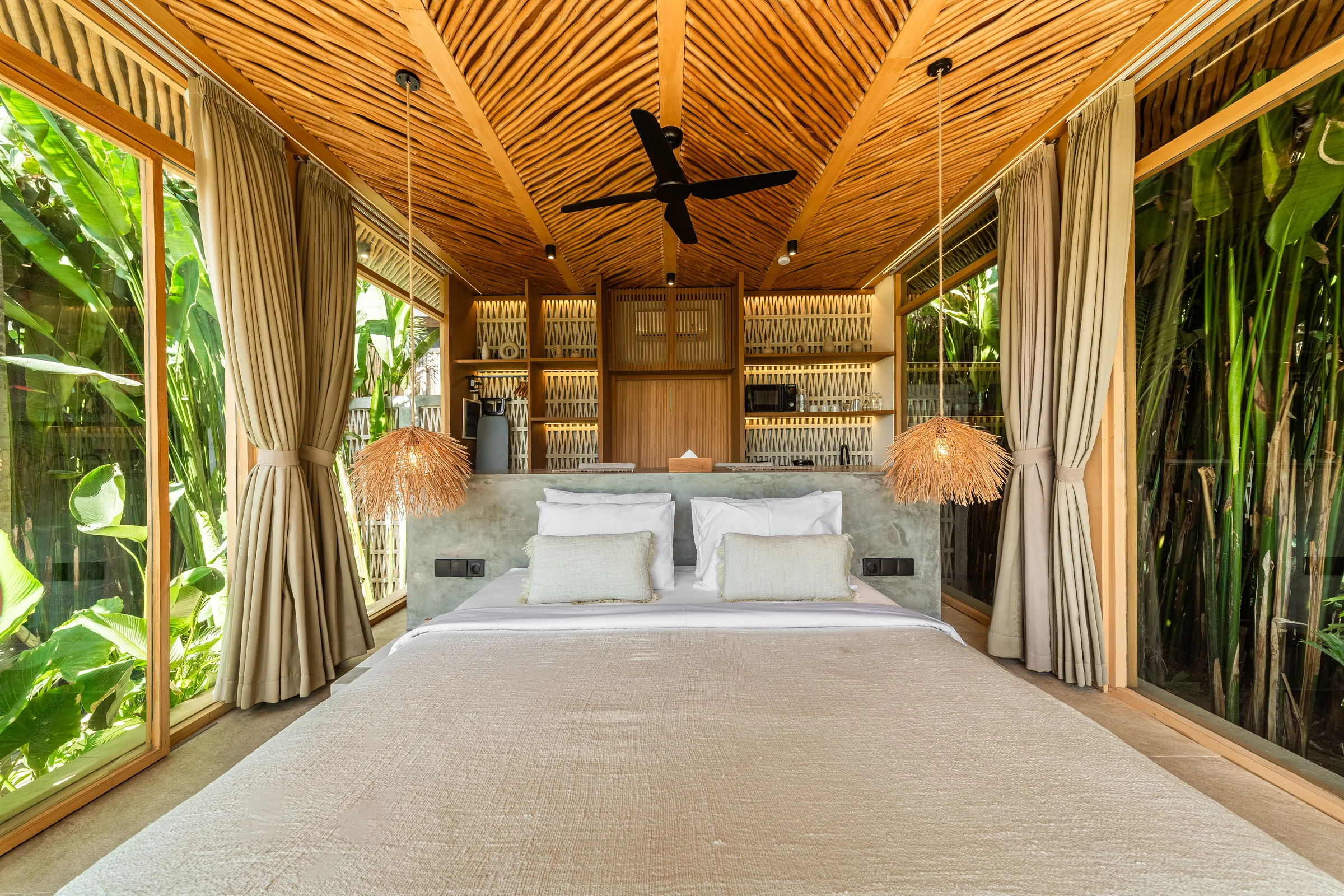 Bedroom under a galam-stick ceiling, with lit timber shelving either side of the bed and glass walls onto the garden