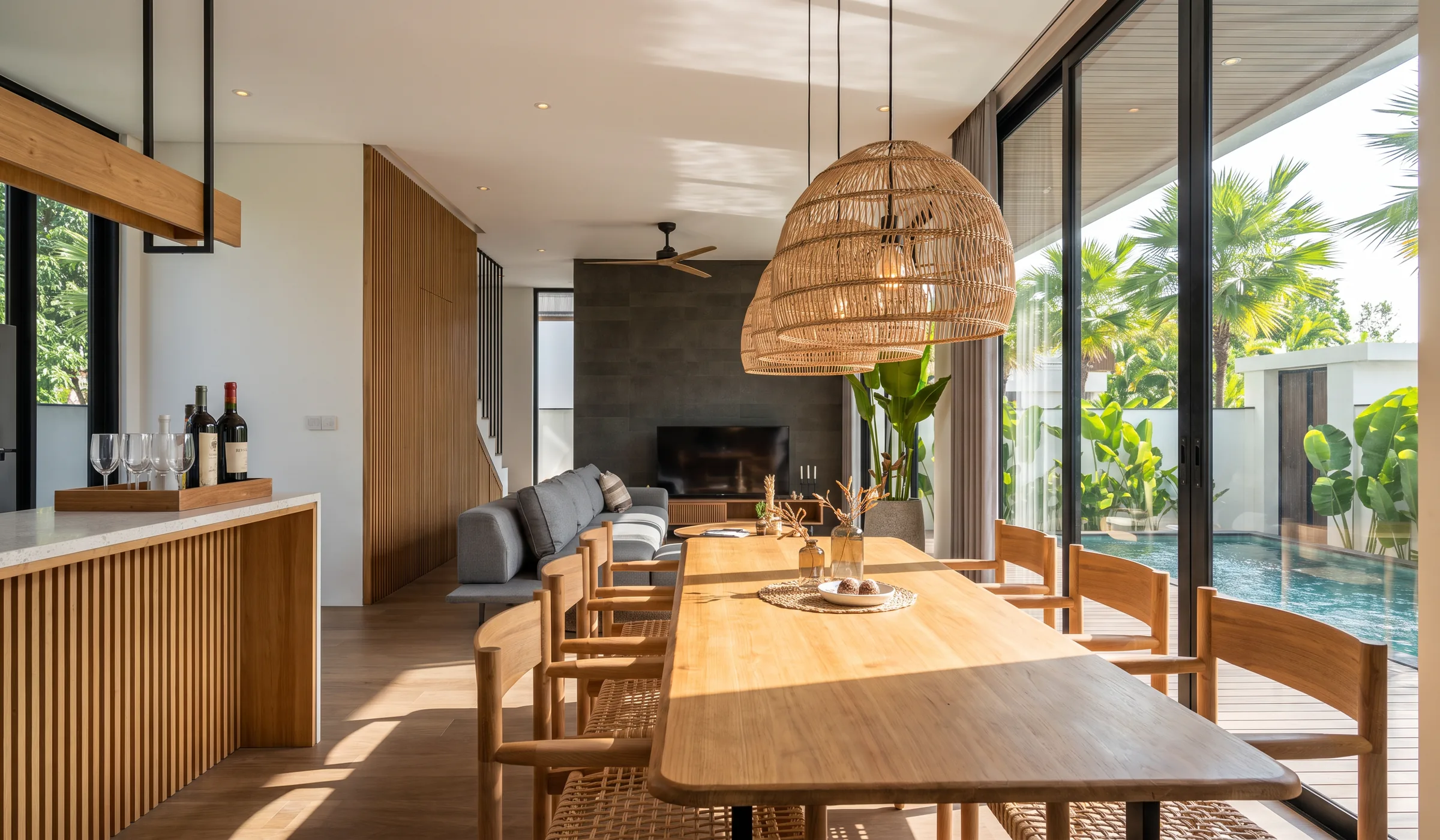 Dining table under woven pendants beside full-height glass doors to the pool, with the living room beyond