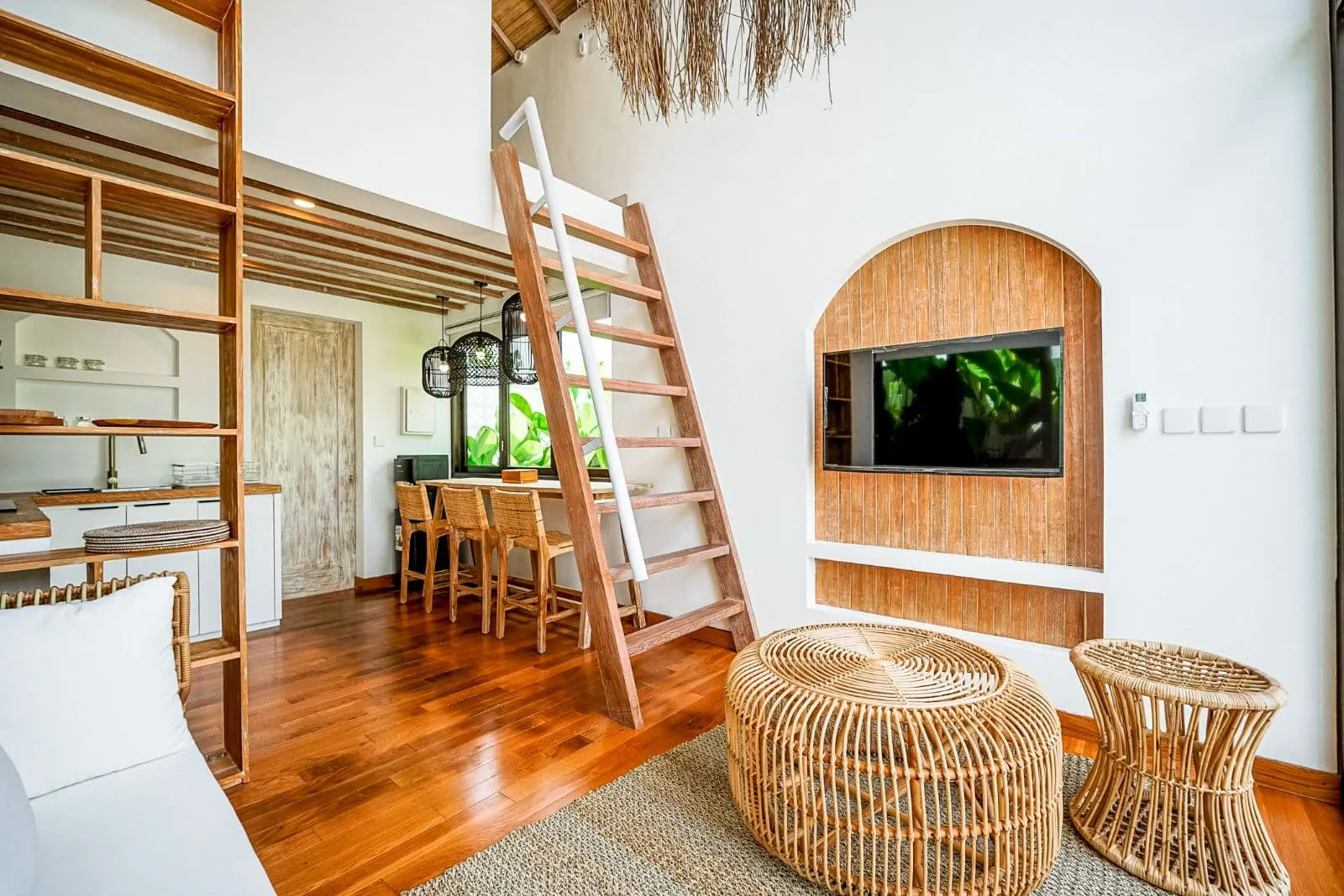 Double-height living room with a mezzanine ladder and woven rattan niche at Villa The Putih